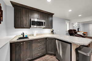 Kitchen featuring dark brown cabinetry, stainless steel appliances, a peninsula, light countertops, and light wood finished floors