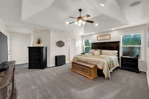 Bedroom with a raised ceiling, carpet flooring, ceiling fan, arched walkways, and recessed lighting