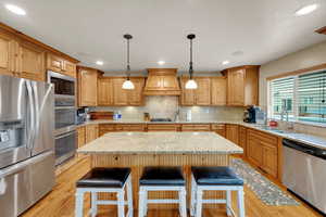 Kitchen featuring stainless steel appliances, a kitchen bar, decorative backsplash, light wood-style flooring, and decorative light fixtures