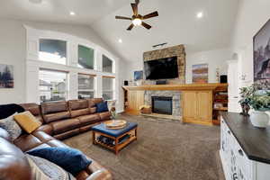 Carpeted living room with high vaulted ceiling, a stone fireplace, a ceiling fan, and recessed lighting