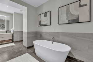 Bathroom featuring a freestanding bath, tile walls, wainscoting, and vanity