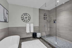 Full bath with a stall shower, a freestanding bath, tile walls, and wainscoting
