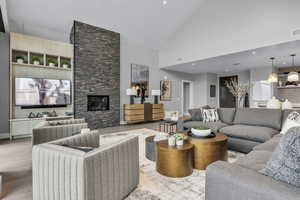 Living area featuring a stone fireplace, high vaulted ceiling, wood finished floors, and recessed lighting