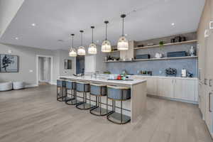 Kitchen featuring a breakfast bar, decorative light fixtures, light brown cabinets, light wood-style floors, and a kitchen island with sink