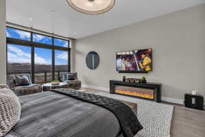 Bedroom featuring expansive windows, wood finished floors, and a glass covered fireplace