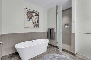 Bathroom featuring a freestanding bath, tile walls, a tile shower, and wainscoting