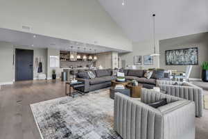 Living area with wood finished floors, a chandelier, high vaulted ceiling, and recessed lighting