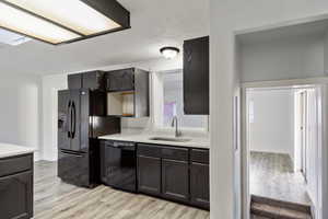 Kitchen with light wood-style floors, black appliances, a textured ceiling, light stone counters, and a skylight