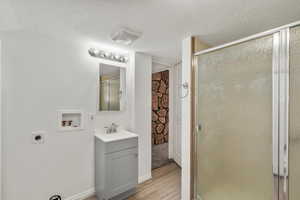 Full bathroom with a shower stall, vanity, a textured ceiling, and light wood finished floors