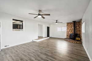 Unfurnished living room with a wood stove, a ceiling fan, and wood finished floors