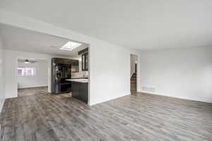 Unfurnished living room with light wood-style floors, a skylight, stairs, and ceiling fan