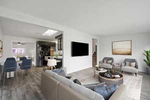 Living area featuring light wood-style floors, stairs, a skylight, and ceiling fan