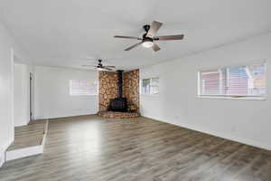Unfurnished living room featuring a wood stove, light wood-style flooring, healthy amount of natural light, and ceiling fan