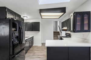 Kitchen featuring dark cabinets, black refrigerator with ice dispenser, light wood finished floors, light stone countertops, and gas stove