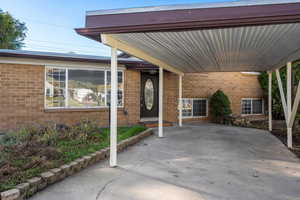 Entrance to property with brick siding and an attached carport