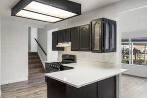 Kitchen featuring black gas range oven, light wood-type flooring, a peninsula, light stone countertops, and under cabinet range hood