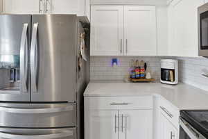 Kitchen featuring appliances with stainless steel finishes, white cabinets, decorative backsplash, and light stone counters