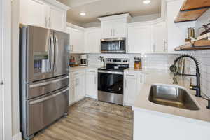 Kitchen with stainless steel appliances, white cabinets, backsplash, light stone counters, and recessed lighting