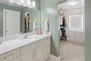 Full bathroom with a spacious closet, vanity, and light carpet