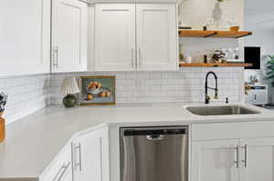Kitchen with stainless steel dishwasher, white cabinetry, open shelves, and backsplash