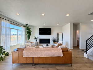 Living area featuring recessed lighting, light wood-style flooring, a glass covered fireplace, a textured ceiling, and stairway