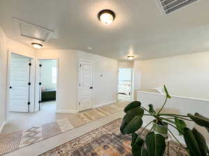 Corridor featuring a textured ceiling, carpet, and attic access