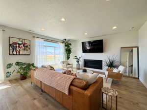 Living room featuring recessed lighting, a textured ceiling, a glass covered fireplace, and light wood finished floors