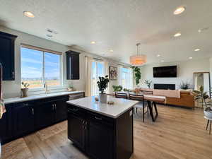 Kitchen with dark cabinetry, light wood-type flooring, a kitchen island, recessed lighting, and a textured ceiling