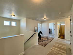 Corridor with an upstairs landing, carpet flooring, and a textured ceiling