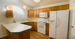 Kitchen with white appliances, hanging light fixtures, a peninsula, light countertops, and dark wood-type flooring