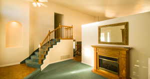 Living area featuring a glass covered fireplace, high vaulted ceiling, and stairway