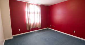 Empty room featuring dark carpet and baseboards