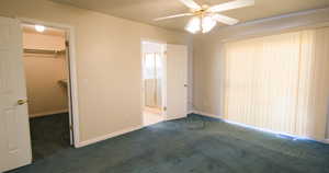 Primary bedroom with a walk in closet, carpet, connected bathroom, and ceiling fan