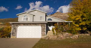 View of front facade with stone siding, a garage, concrete driveway, and a mountain view