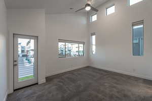 Spare room featuring plenty of natural light, dark carpet, a high ceiling, and a ceiling fan