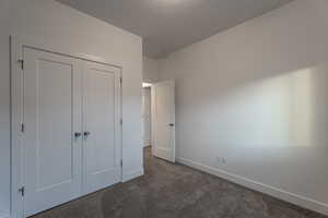 Unfurnished bedroom with dark carpet, a closet, and a textured ceiling