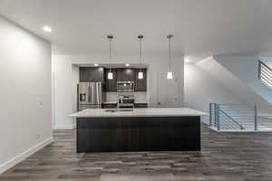 Kitchen with dark brown cabinetry, appliances with stainless steel finishes, a kitchen island with sink, decorative backsplash, and decorative light fixtures