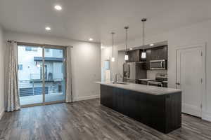Kitchen with stainless steel appliances, decorative light fixtures, dark wood finished floors, a center island with sink, and recessed lighting