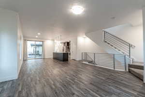 Unfurnished living room with stairway, dark wood-type flooring, a textured ceiling, and recessed lighting