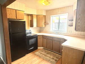 Kitchen with black appliances, light countertops, wallpapered walls, light wood-style flooring, and a textured ceiling