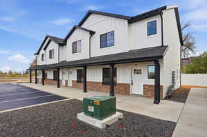 Modern farmhouse featuring board and batten siding, brick siding, a shingled roof, a porch, and uncovered parking