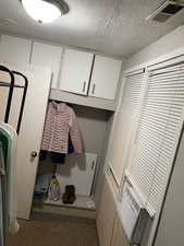 Laundry area with a textured ceiling and light carpet. APT 1