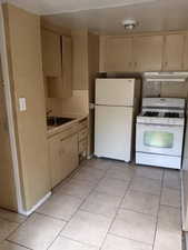 Kitchen with cream cabinetry, white appliances, light countertops, light tile patterned floors, and tasteful backsplash. APT 3