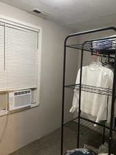 Unfurnished bedroom with a textured ceiling, dark colored carpet, and cooling unit. APT 1