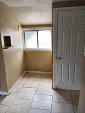Hallway with a textured wall, light tile patterned flooring, and vaulted ceiling. APT 3