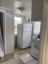 Kitchen featuring white appliances, a textured wall, light tile patterned flooring, and a textured ceiling