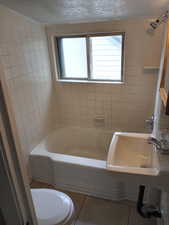 Bathroom featuring tile patterned flooring, tub / shower combination, and a textured ceiling. APT 3