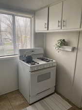 Kitchen with gas range gas stove, light tile patterned flooring, white cabinetry, and light countertops
