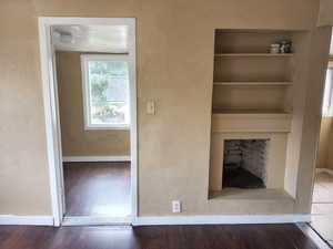 Unfurnished living room featuring a textured wall, wood finished floors, and built in shelves. APT 3