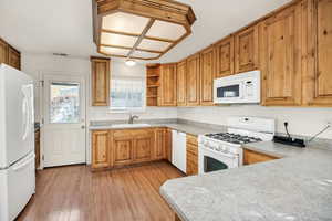 Kitchen featuring open shelves, white appliances, light wood-style floors, light countertops, and brown cabinets